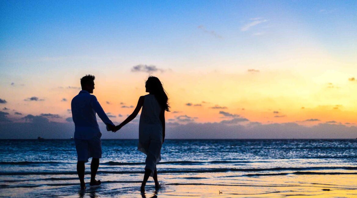 man and woman holding hands walking on seashore during sunrise