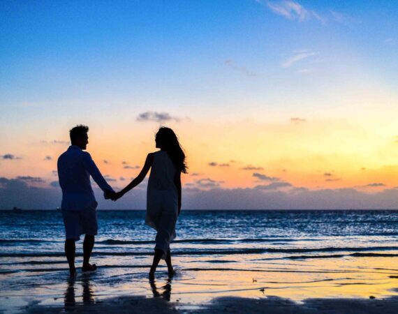 man and woman holding hands walking on seashore during sunrise